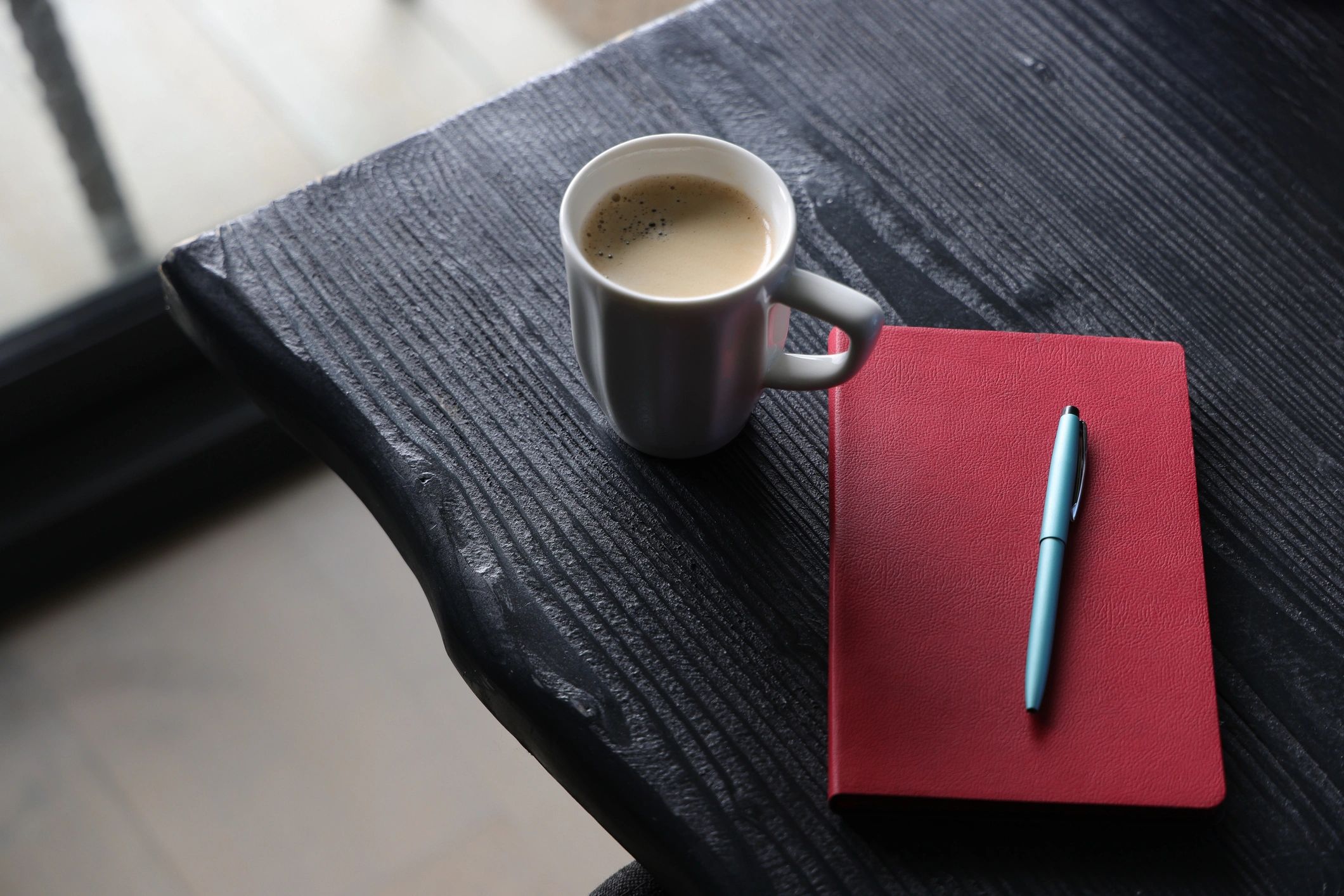 Cuaderno rojo, bolígrafo y taza de café sobre una mesa